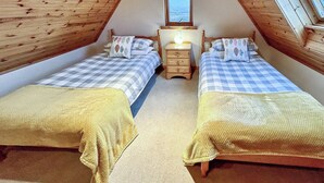 A cozy attic bedroom with two beds, a nightstand, and a window.