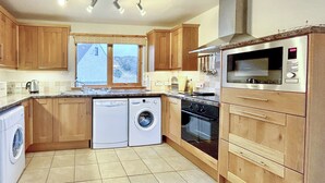 A modern kitchen with wooden cabinets, a built-in oven, a microwave, and a washing machine.
