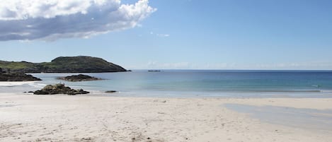 Una spiaggia con impronte, acqua calma e un'isola in lontananza.