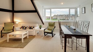 Una sala de estar moderna con comedor, ventanas amplias y vistas a edificios residenciales.