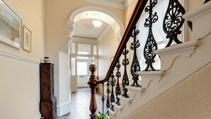 Una imponente escalera con barandillas negras decorativas, un suelo de baldosas con diseño y una pared blanca con un cuadro enmarcado.