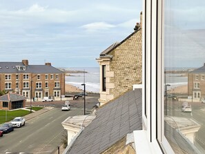 Eine Küstenstadt mit Blick auf das Meer, eine Straße mit Autos und Gebäude mit Fassaden aus Backstein und Naturstein.