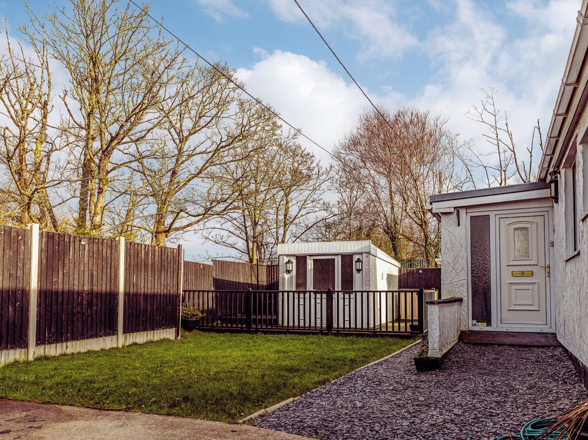 A residential area with a wooden fence, a small shed, and a house with a white door.