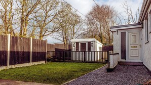 Ett bostadsområde med ett trästaket, ett litet förråd och ett hus med en vit dörr.