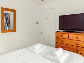 A hotel room with a bed, a wooden dresser with a television, and a mirror on the wall. - 3 bedroom accommodation in Flookburgh (Flookburgh)