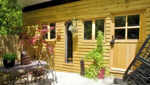 Une maison en bois avec un patio, une table et des chaises, une lanterne suspendue et des plantes en pot.