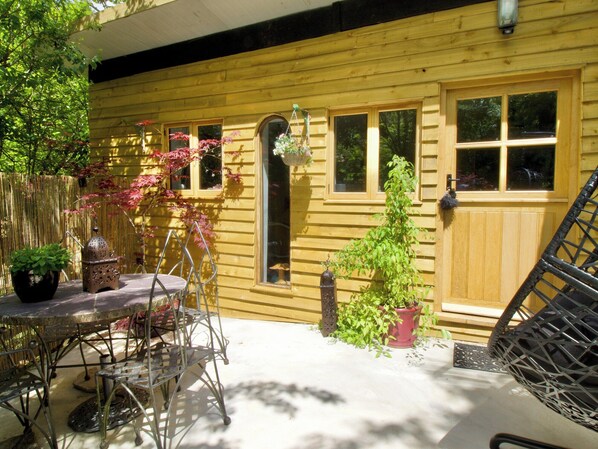 Une maison en bois avec un patio, une table et des chaises, une lanterne suspendue et des plantes en pot.