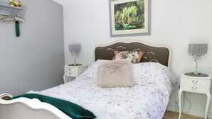 Une chambre à coucher comprenant un lit, deux tables de chevet, une étagère fixée au mur et un tableau encadré.