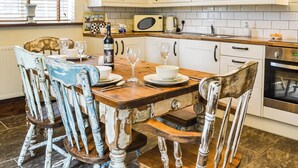 Una cocina con armarios blancos, una mesa de madera y sillas. Hay una botella de vino y copas sobre la mesa.