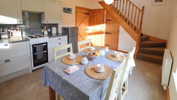 Een keuken met een eettafel voor vier personen, houten stoelen, een trap en uitzicht op het buiten.