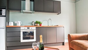 Una cocina moderna con horno empotrado, cafetera y lavabo. Hay una mesa de madera con una botella de champán y copas.