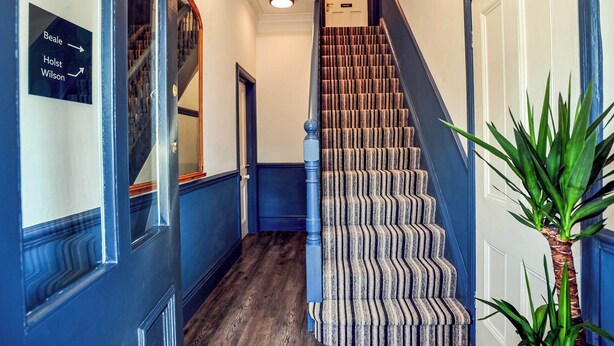 Una escalera con alfombra a rayas, escalones de madera y pared azul.