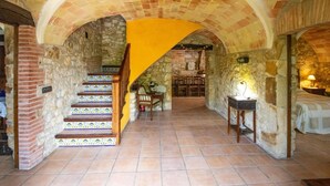 A stone-walled hallway with a tiled staircase leading to a room with a bed and a table.