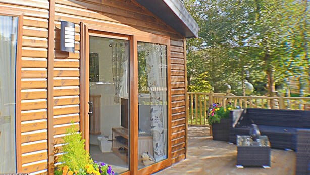 Eine Holzhütte mit Glastür, die in einen Innenraum mit einer Couch und einem Fernseher führt.