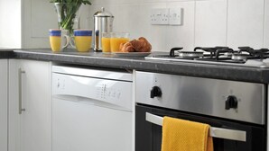A kitchen with a dishwasher, a stove, and a yellow towel hanging on the oven door. - 1 bedroom accommodation in Cheltenham (Cheltenham)
