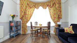 A dining area with a wooden table, four chairs, and a bookshelf with books and a vase of flowers. - 1 bedroom accommodation in Cheltenham (Cheltenham)