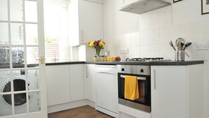 A modern kitchen with white cabinets, a wooden floor, a stove, and a window with a view of greenery outside. - 1 bedroom accommodation in Cheltenham (Cheltenham)