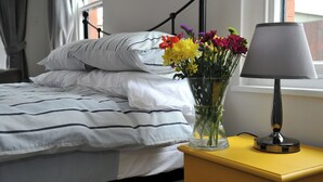 A neatly made bed with striped bedding, a vase of flowers on a bedside table, and a lamp. - 1 bedroom accommodation in Cheltenham (Cheltenham)