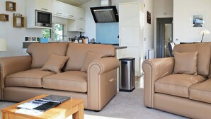 A modern living room with a beige sofa set, a wooden coffee table, and a kitchen in the background. - 3 bedroom accommodation in Brynteg, near Benllech (Brynteg, near Benllech)
