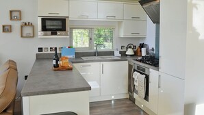 A modern kitchen with white cabinetry, a built-in microwave, a stove, and a window with blinds. - 3 bedroom accommodation in Brynteg, near Benllech (Brynteg, near Benllech)