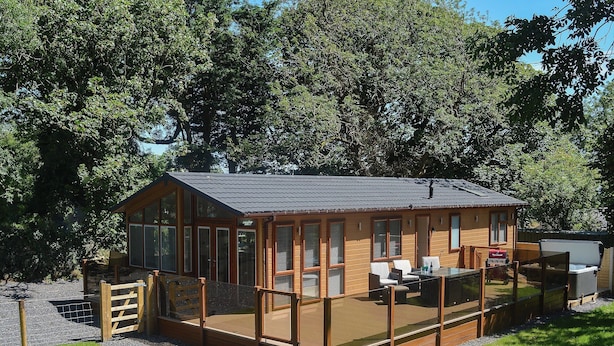 A wooden cabin with a deck, large windows, and a covered patio area. - 3 bedroom accommodation in Brynteg, near Benllech (Brynteg, near Benllech)