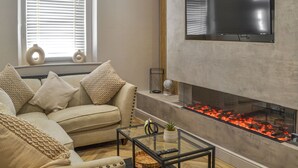 A modern living room with a beige sofa, a glass coffee table, and a fireplace with red embers. - 2 bedroom accommodation in Morpeth (Morpeth)