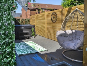 Un jardin avec une terrasse en bois, un fauteuil suspendu, un barbecue et une clôture en bois.