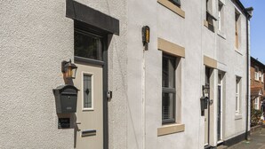 A two-story building with a textured facade, a door with a small window, and a mailbox. - 2 bedroom accommodation in Morpeth (Morpeth)