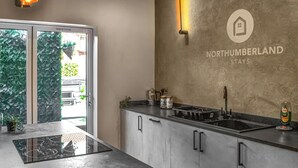 A modern kitchen with a large island, a built-in oven, and a sink. There's a sign on the wall that reads "Northumberland Stays". - 2 bedroom accommodation in Morpeth (Morpeth)