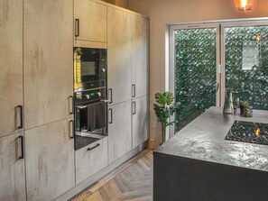 Une cuisine moderne dotée d’appareils électroménagers intégrés, d’une grande fenêtre offrant une vue sur la verdure, et d’un plan de travail agrémenté d’une plante et d’un vase.