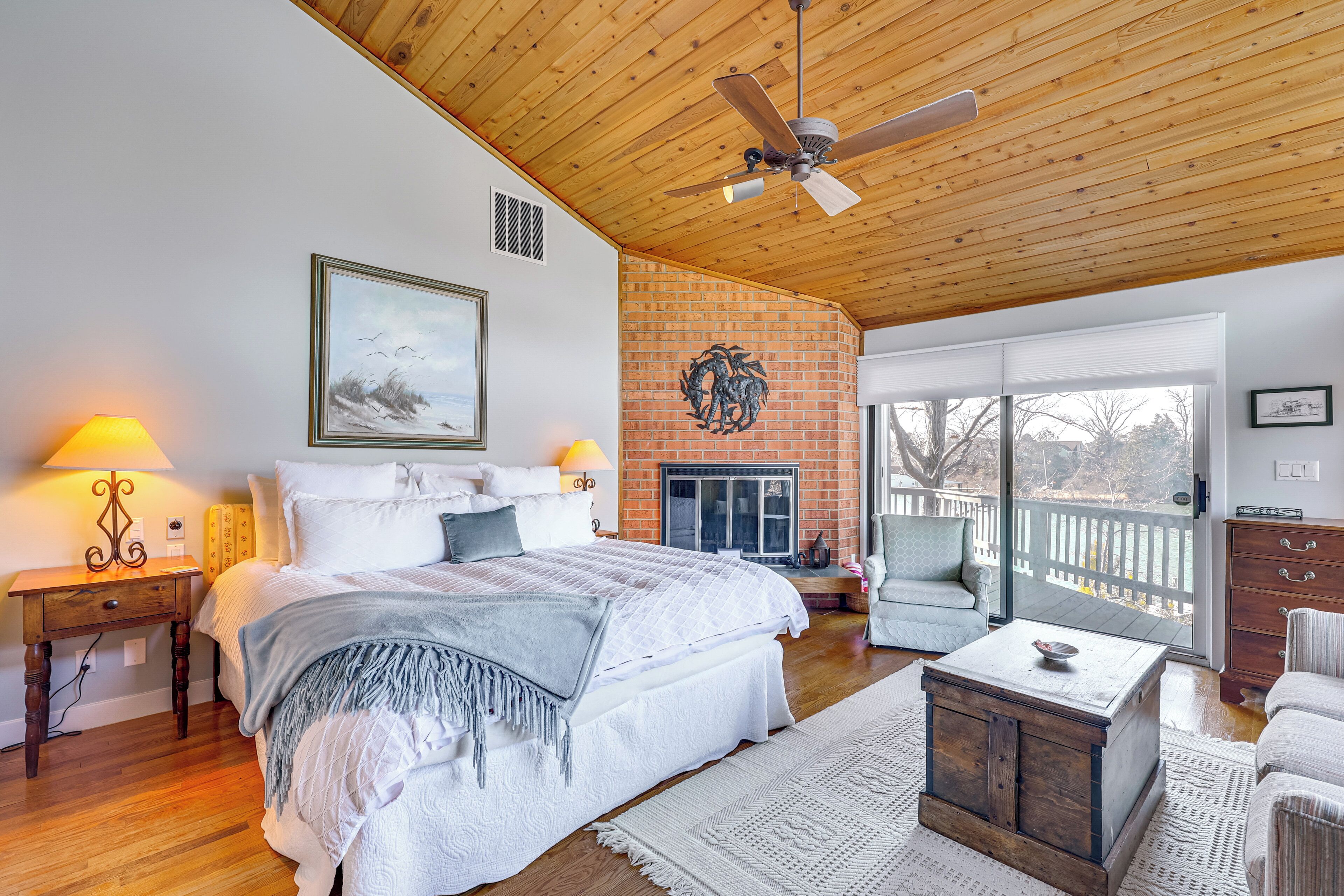 A bedroom with a large bed, a wooden ceiling, a fireplace, and a balcony with a view.