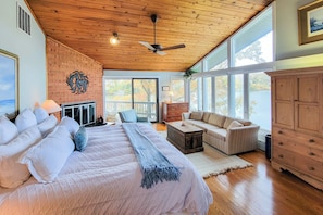 Un dormitorio amplio con una cama grande, un ventilador de techo y vistas a un lago a través de amplios ventanales.