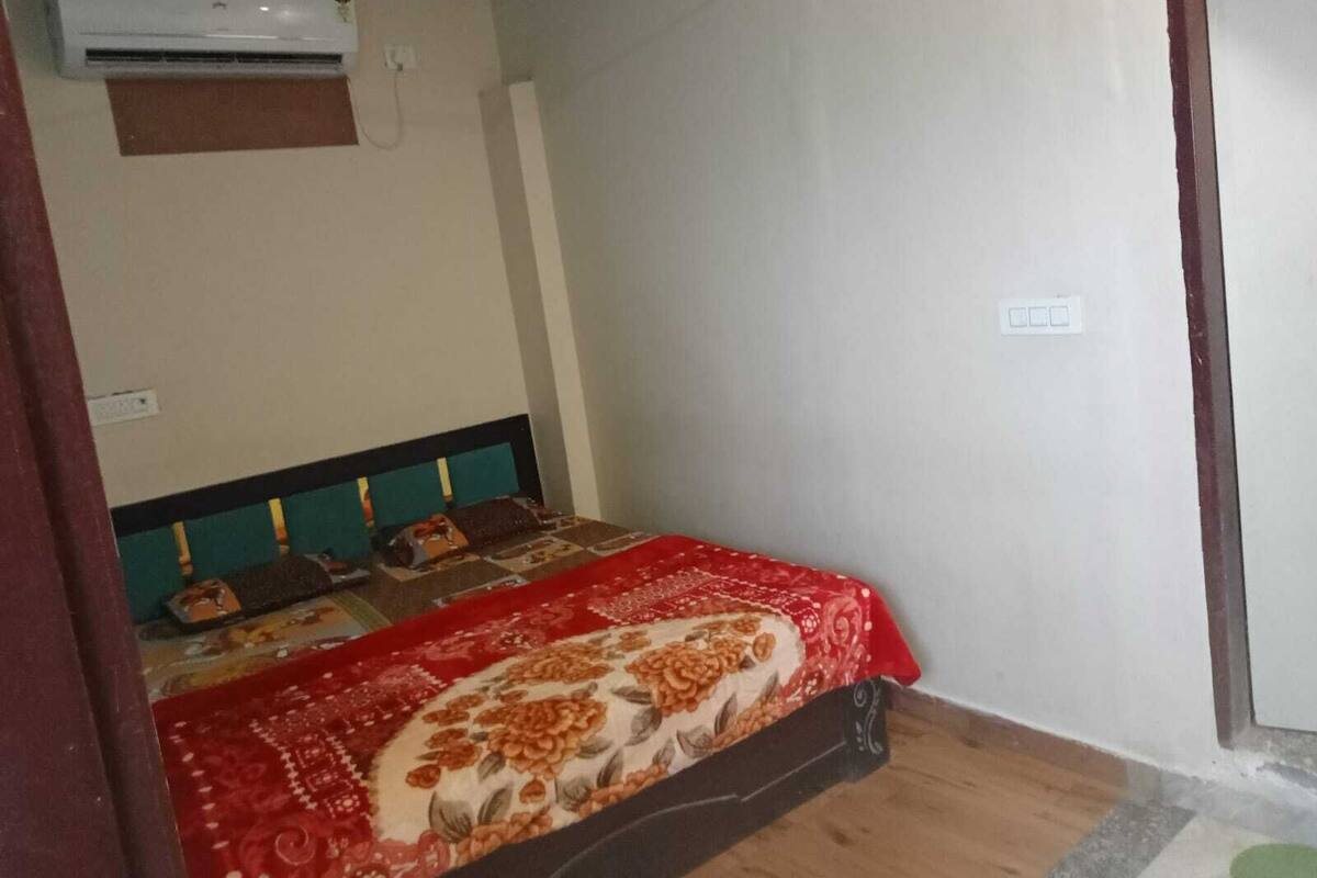 A bedroom with a bed, an air conditioner, and a wall socket.