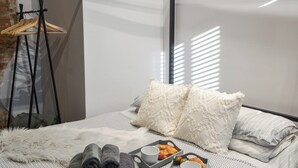 A neatly made bed with rolled towels, pillows, and a tray with croissants and a cup.