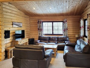 L’intérieur d’une cabane en rondins, avec un ensemble de meubles en cuir, un téléviseur et une fenêtre avec des rideaux.