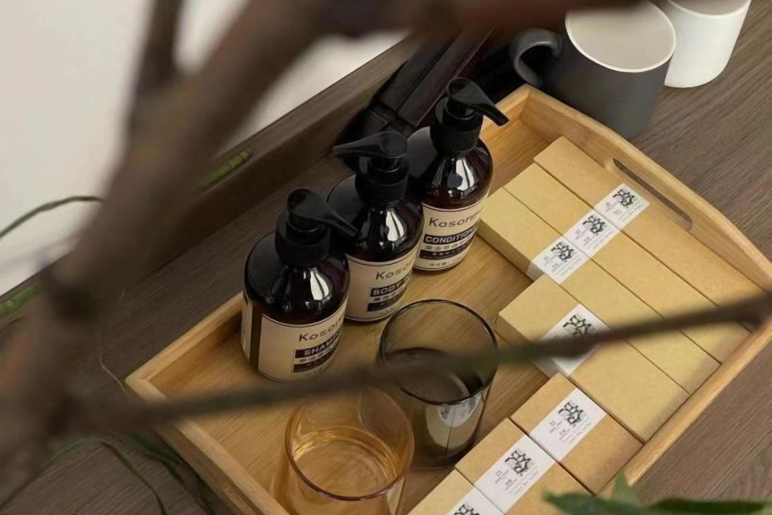 A wooden tray with three bottles of body lotion and a glass on a wooden surface.