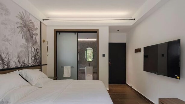 Habitación de hotel con una cama grande, un televisor de pantalla plana, un cuadro en la pared y un baño visible a través de una puerta de cristal.