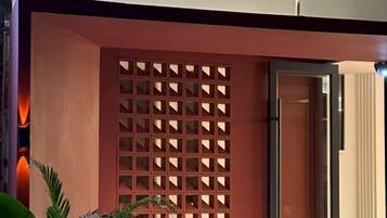 A hotel entrance with a red facade, a grid-patterned wall, and a door leading inside.