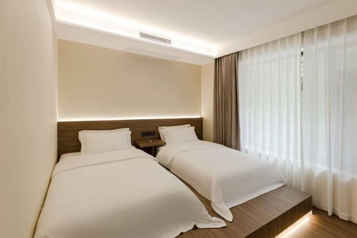 A hotel room with two beds, a wooden headboard, a nightstand, and sheer curtains.