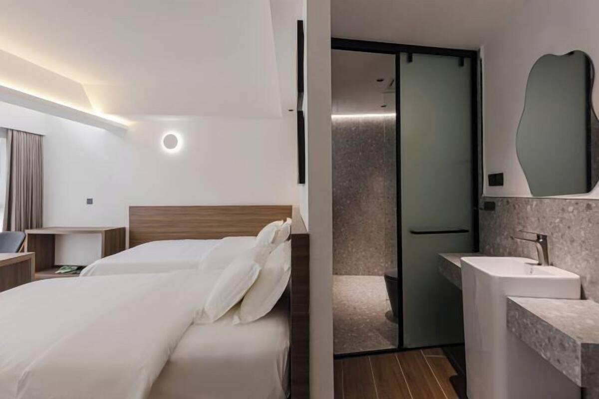 A modern hotel room with a bed, bedside table, and a bathroom with a sink and mirror.