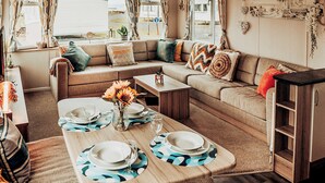 A cozy RV interior with a sectional sofa, a dining table set for four, and a large window offering a view of the outdoors. - A perfect family coastal break in the heart of Ayrshire. (Ayr)