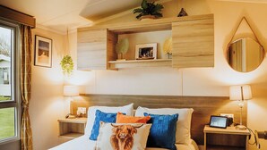 A neatly arranged hotel room with a bed, bedside tables, a mirror, and a window with curtains. - A perfect family coastal break in the heart of Ayrshire. (Ayr)