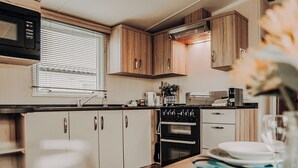A compact kitchen with wooden cabinets, a microwave, a stove, and a sink. - A perfect family coastal break in the heart of Ayrshire. (Ayr)