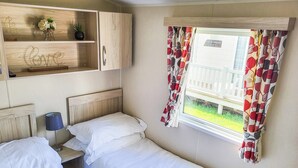 Une chambre avec deux lits, une étagère en bois ornée d’objets décoratifs et une fenêtre avec des rideaux.