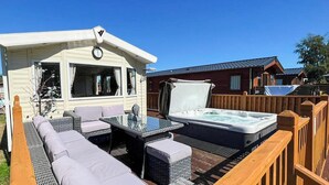 Une caravane dotée d’un espace extérieur aménagé avec un jacuzzi, des sièges de jardin et une terrasse en bois.