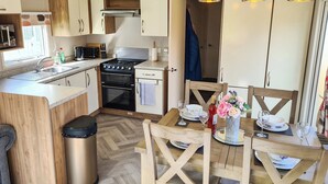Une cuisine de taille réduite, équipée d’une cuisinière, d’un évier et de meubles de rangement en bois. On y trouve une table à manger avec des chaises et une poubelle.
