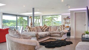 A spacious living room with a large sectional sofa, a red armchair, and a black furry rug. - 5 bedroom accommodation in Rudyard Lake (Rudyard Lake)