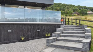 A modern building with a glass facade, stone steps, and a wooden fence. - 5 bedroom accommodation in Rudyard Lake (Rudyard Lake)