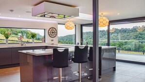 A modern kitchen with a central island, bar stools, and large windows offering a view of the countryside. - 5 bedroom accommodation in Rudyard Lake (Rudyard Lake)
