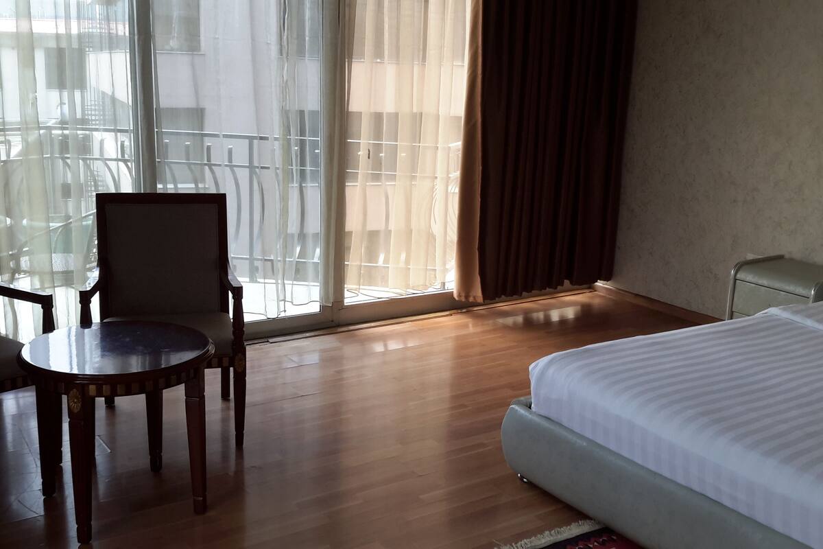 A hotel room with a bed, a chair, a small table, and a window with curtains.